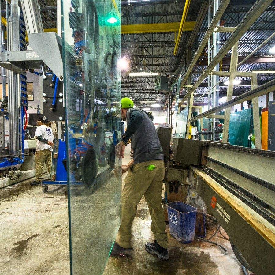 A worker in our fabrication facility worker moving a large piece of glass. A recycling bin sits next to him.
