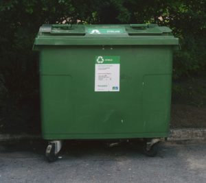 Green recycling bin on asphalt in front of forestry