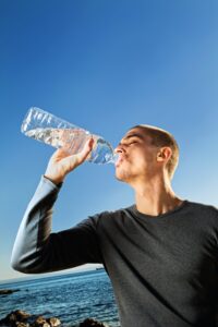 Man is long-sleeved grey shirt drinking water from botle