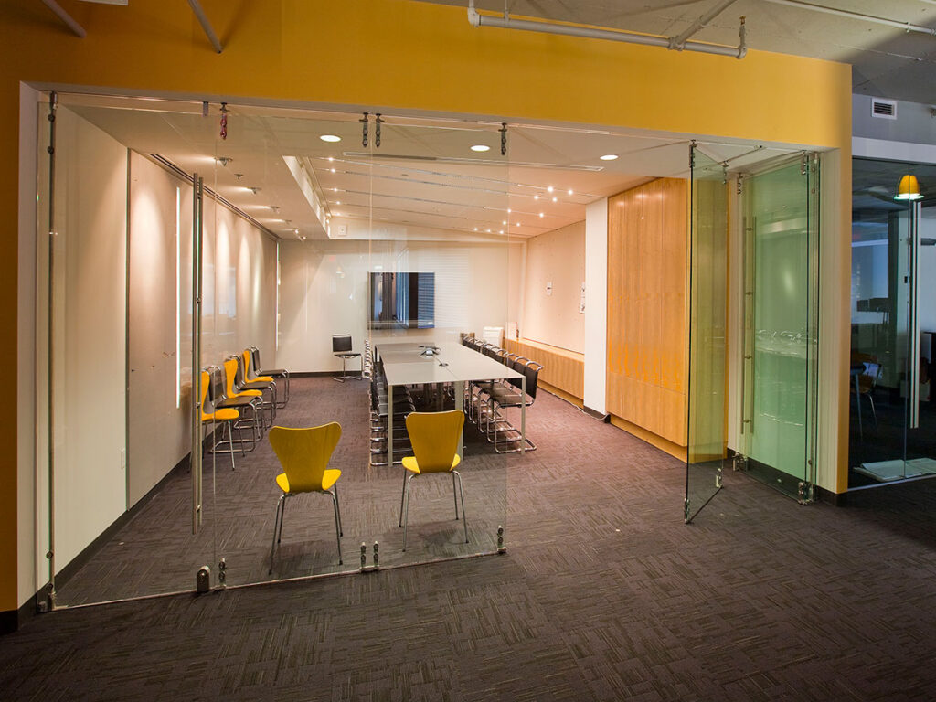 The HNTB headquarters. An office meeting room with yellow and brown chairs, a yellow wall, and a foldable glass wall divider.