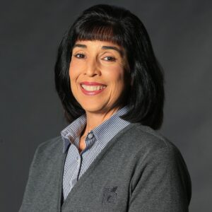 Cindy French, one of KGa's Women in Construction. Our Vice President of Human Resources. A tan woman with dark black hair, a button up shirt, and grey sweater.